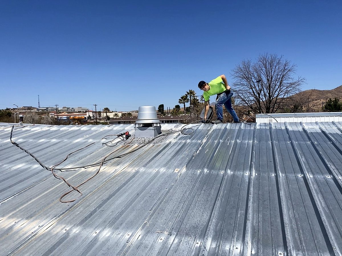 Crew member spraying coating on a ribbed metal roof