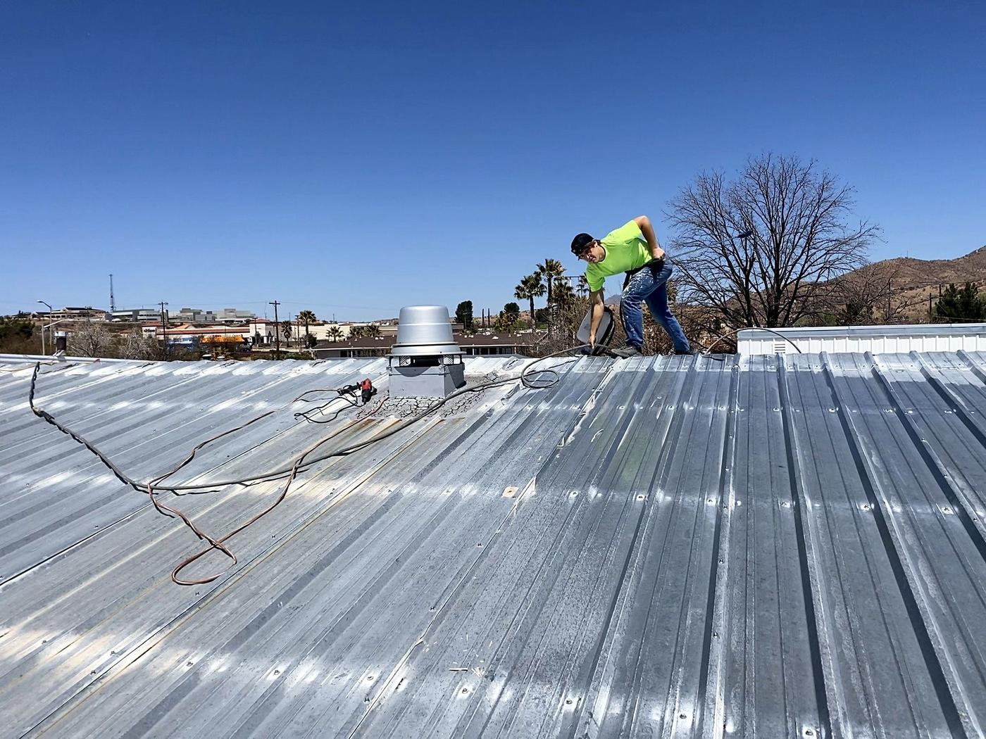Crew member spraying coating on a ribbed metal roof