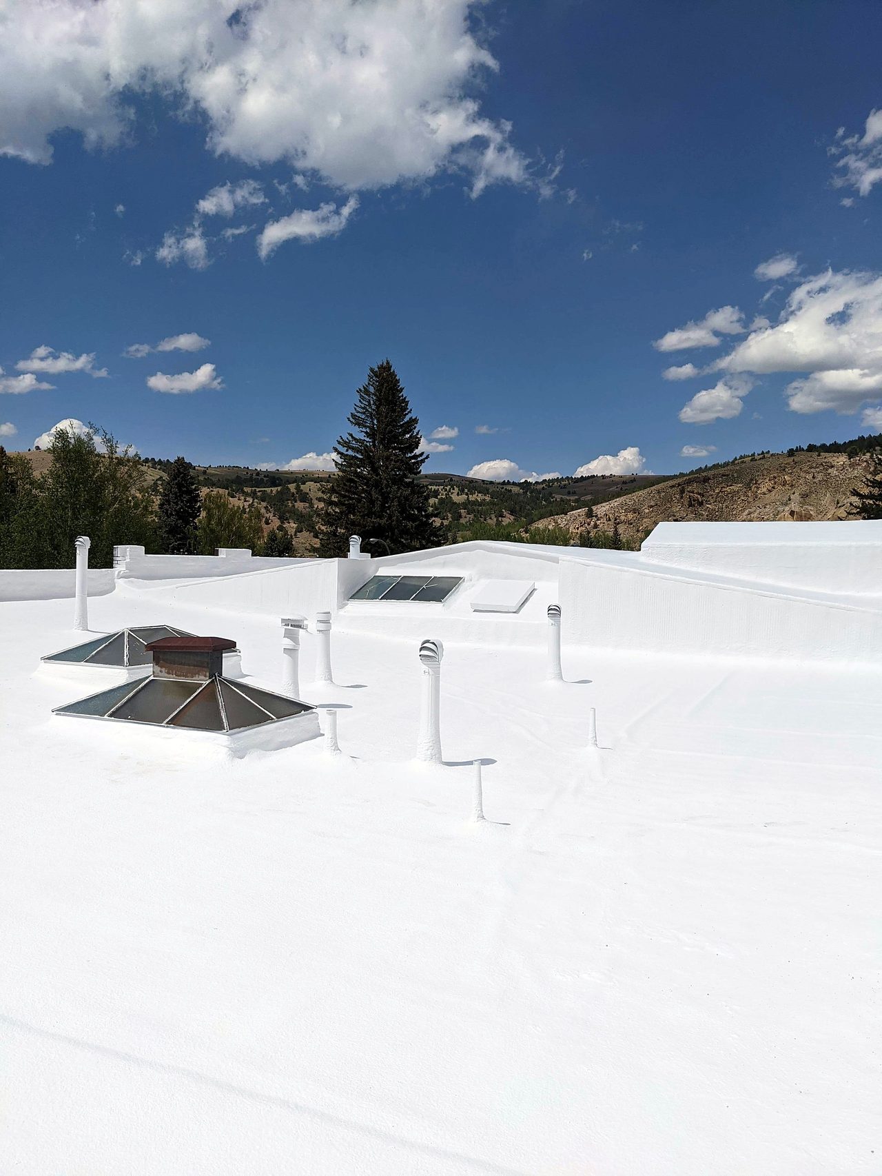Finished white coated flat roof with rooftop vents and a mountain view