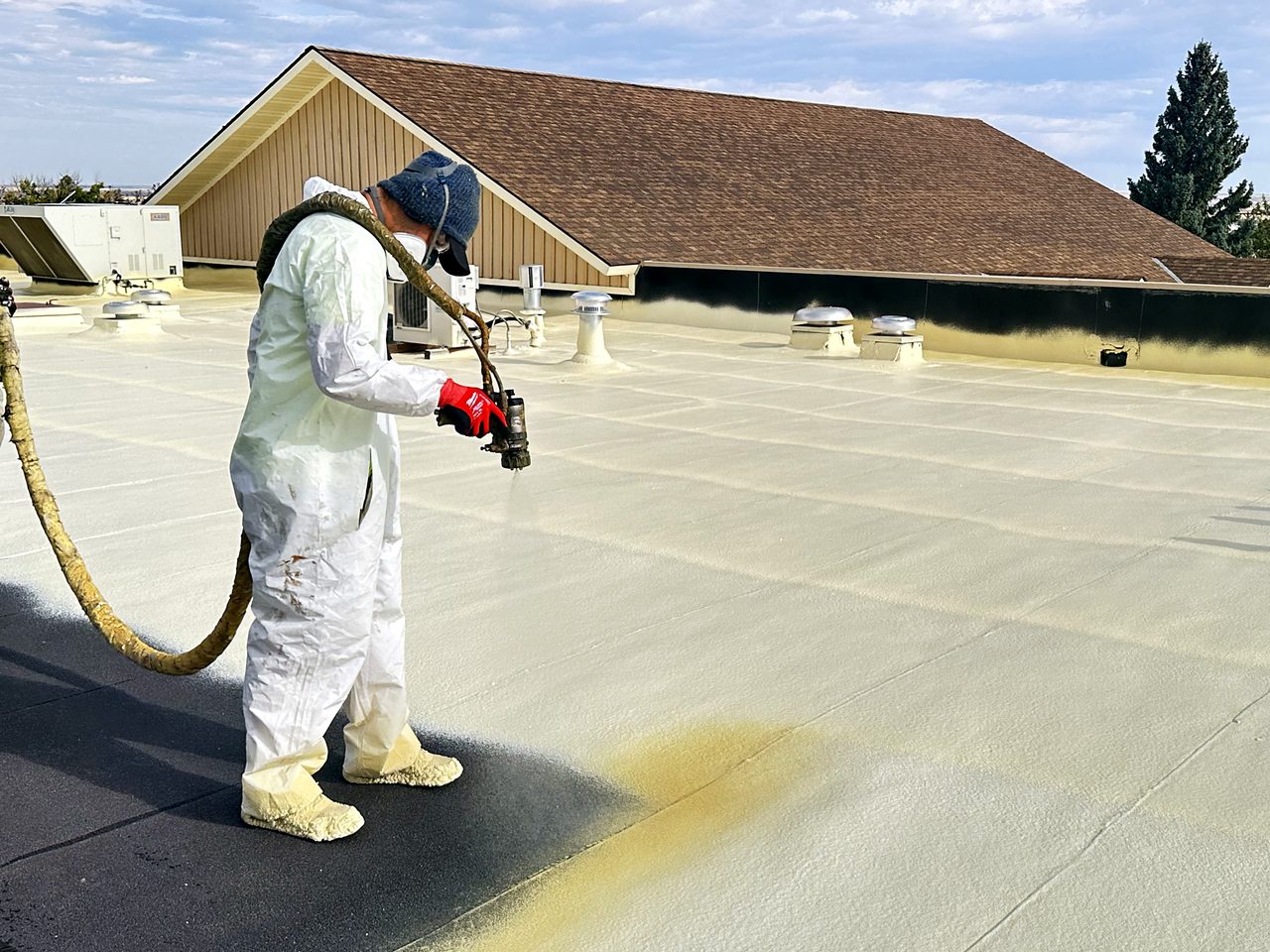 Crew member in a protective suit spray-applying roof coating for the City of Cut Bank, Montana